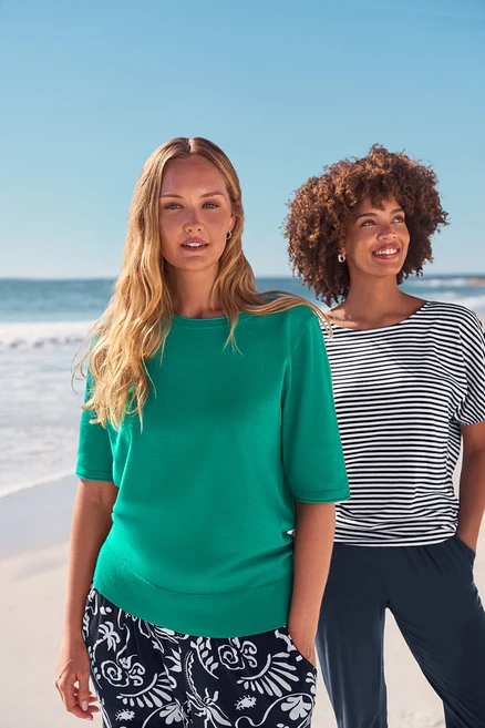 Deux femmes sur la plage portent des boucles d’oreilles avec pierres de cristal de verre, des créoles pavé et un pantalon pour femme 3/4 en jersey, bleu foncé.