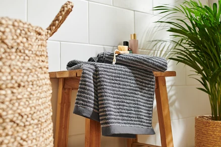 Deux linges de toilette anthracite de haute qualité sont posés sur un tabouret en bois.