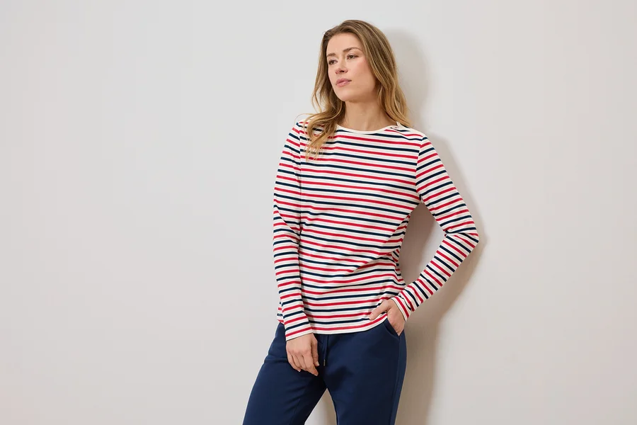 Femme portant un t-shirt rayé à manches longues et un pantalon de jogging bleu, une main dans la poche.
