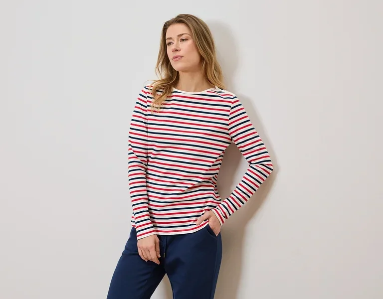 Femme portant un t-shirt rayé à manches longues et un pantalon de jogging bleu, une main dans la poche.