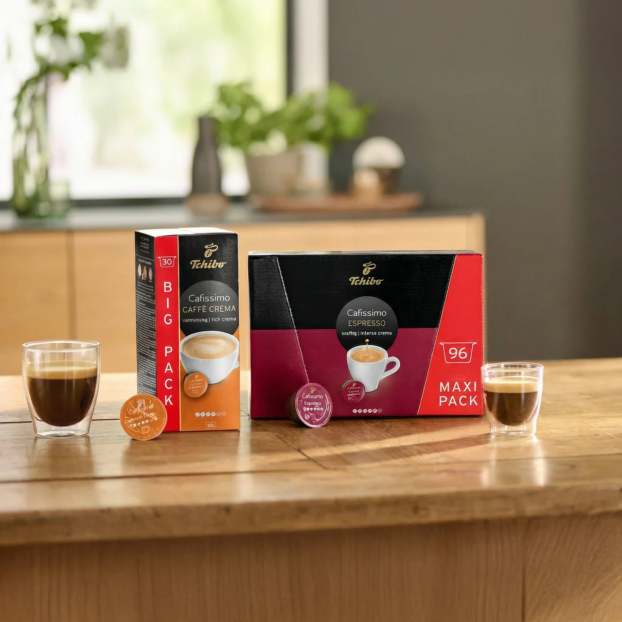 Sur une table en bois, deux verres à expresso sont posés à côté des paquets Tchibo Cafissimo Caffe Crema et Espresso.