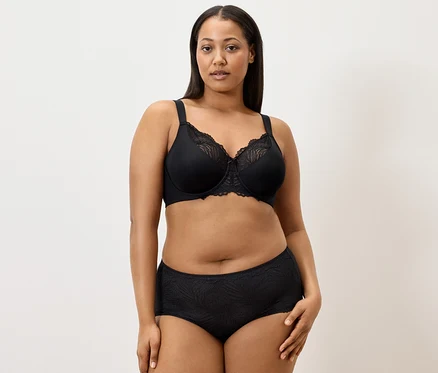 Une femme porte un soutien-gorge minimiseur noir et 5 culottes noires sur un fond blanc.