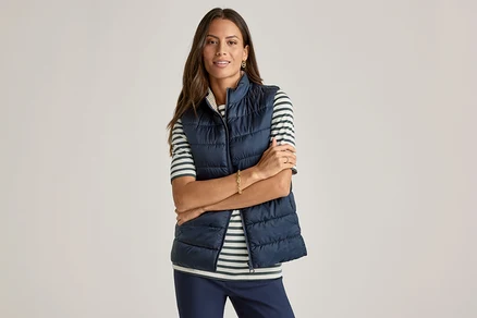 Une femme les bras croisés porte un gilet bleu marine sur un T-shirt demi-manches, vert à rayures.