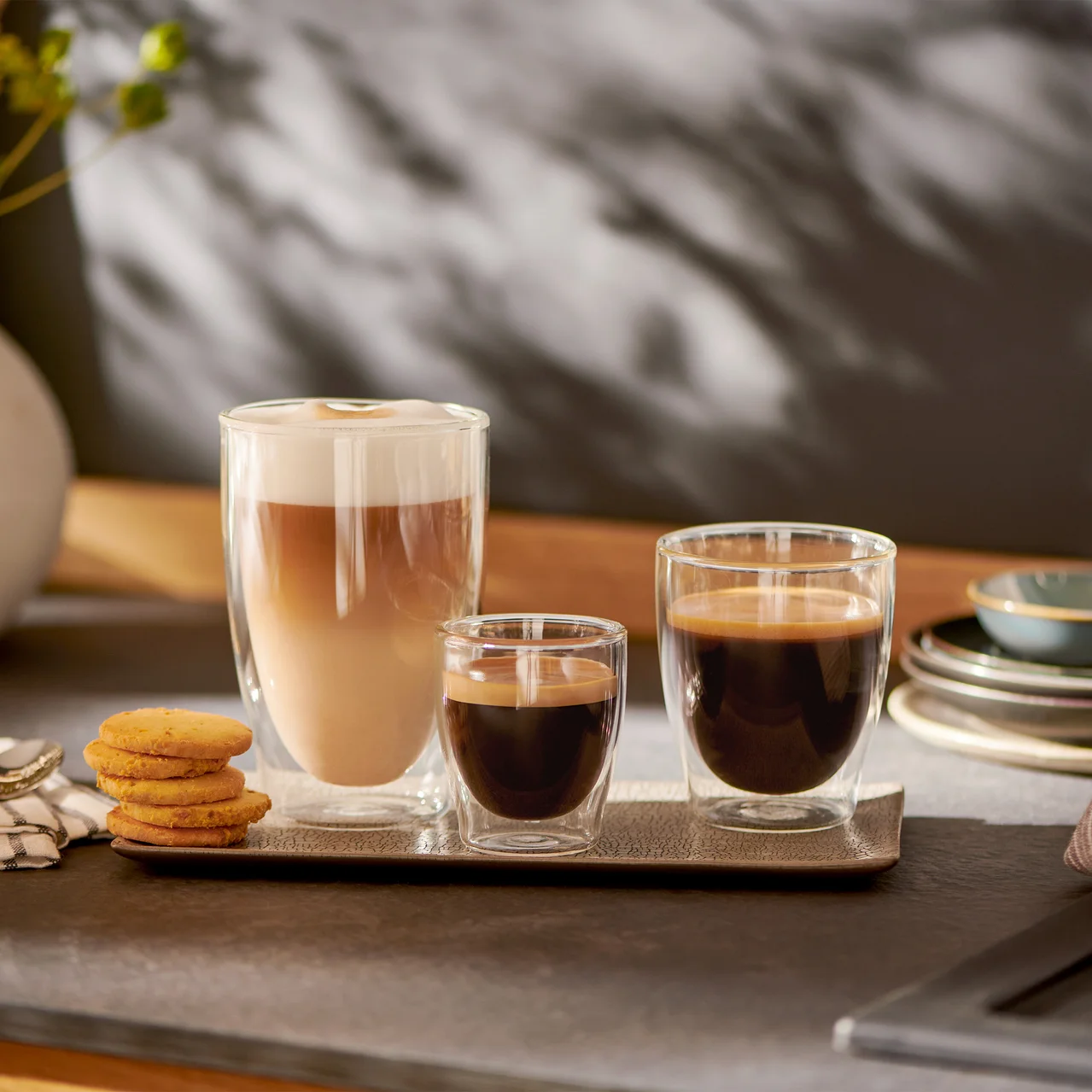 Trois verres de café côte à côte sur un plateau. Un cappuccino à gauche, un expresso au milieu et un café à droite.