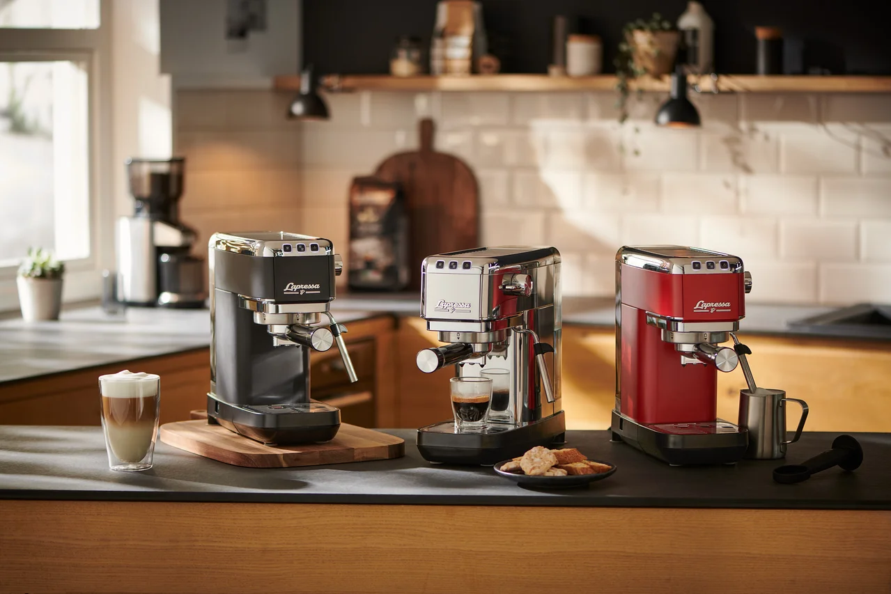 Trois machines à porte-filtre « Lapressa » (noire, argentée et rouge) sont posées sur un comptoir de cuisine. La machine argentée prépare un expresso.