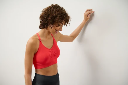 Une femme appuyée contre un mur porte une brassière de sport Seamless rouge.