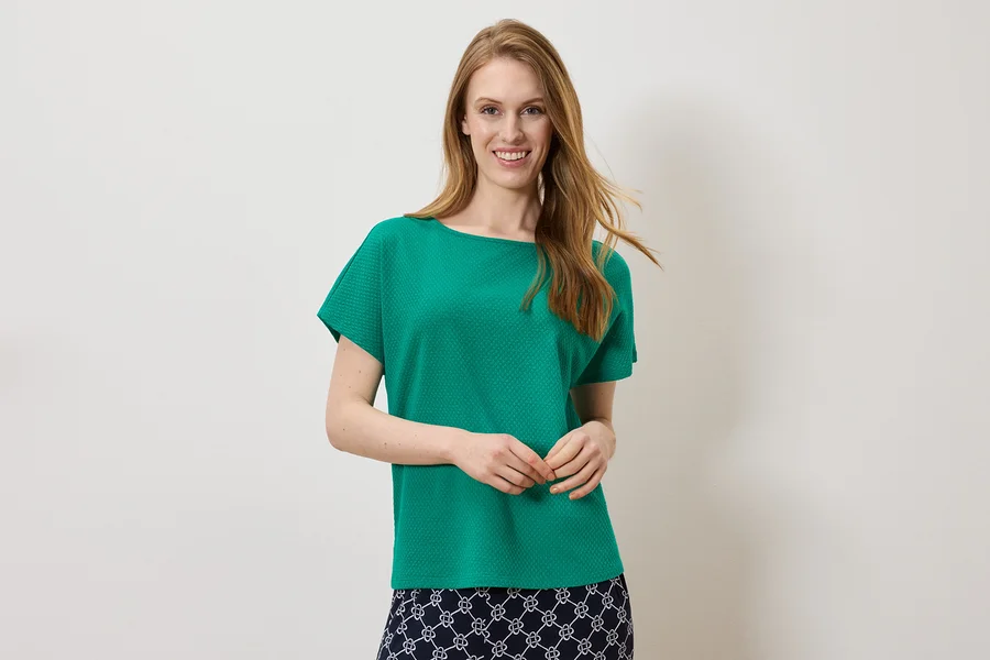 Femme souriante portant un haut vert et une jupe avec un motif blanc et bleu marine.