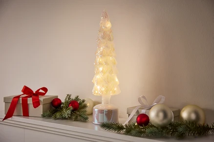 Un arbre décoratif illuminé se dresse entre des cadeaux et des décorations.