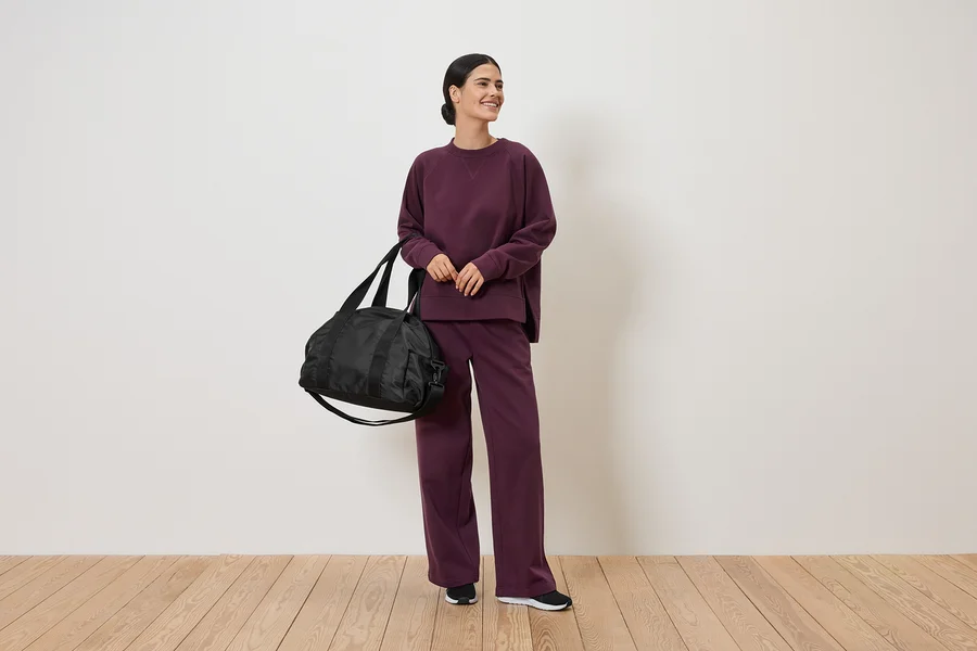 Femme en survêtement bordeaux tenant un sac de sport noir.