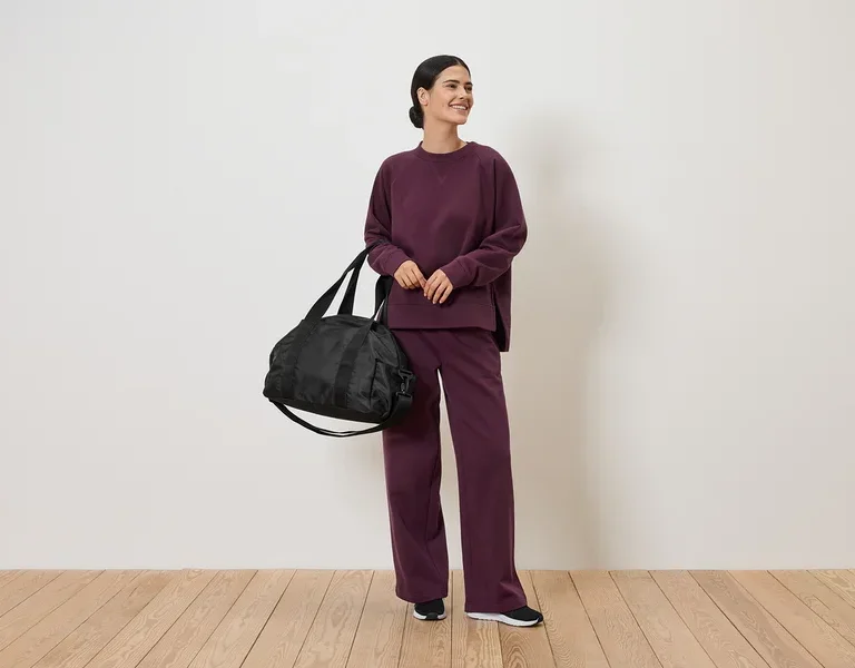 Femme en survêtement bordeaux tenant un sac de sport noir.