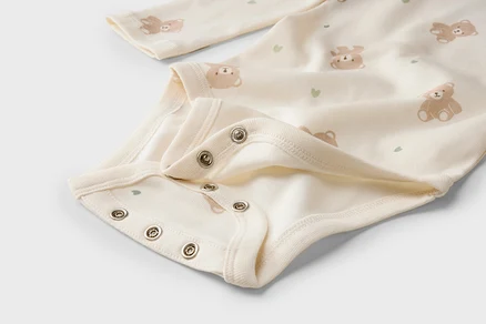 Gros plan d'un body clair pour bébé avec motif oursons et cœurs, et boutons-pression à l'entrejambe.