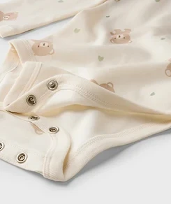 Gros plan d'un body clair pour bébé avec motif oursons et cœurs, et boutons-pression à l'entrejambe.