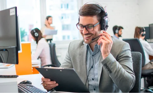 Un homme avec un casque souriant tient un presse-papiers dans un bureau.
