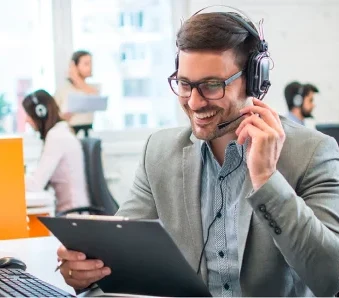 Un homme avec un casque souriant tient un presse-papiers dans un bureau.