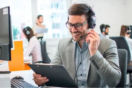 Un homme avec un casque souriant tient un presse-papiers dans un bureau.