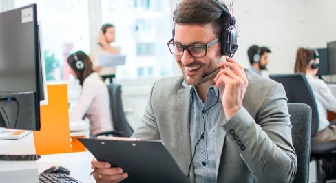 Un homme avec un casque souriant tient un presse-papiers dans un bureau.