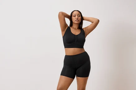 Femme posant en soutien-gorge de sport noir et short noir, les mains jointes derrière la tête.