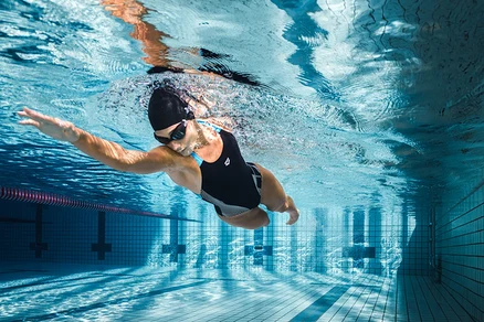 Une femme nage sous l'eau dans une piscine et porte un maillot de bain noir Swim Pro Back Bustier Lily arena Feel.