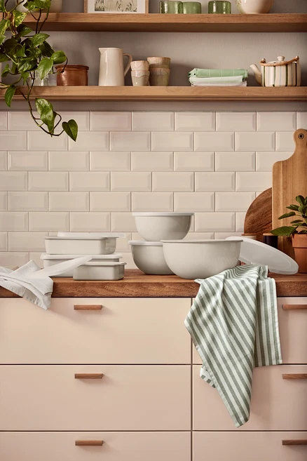Trois plats de service et de préparation en émail et trois plats de cuisson émaillés avec couvercle sont posés sur un comptoir de cuisine. Un torchon rayé pend sur le bord.