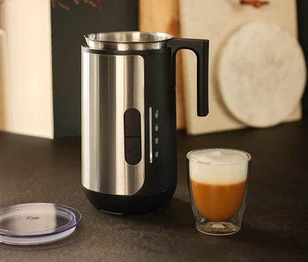 Un mousseur à lait en acier inoxydable est posé à côté d'un verre de café avec de la mousse de lait.