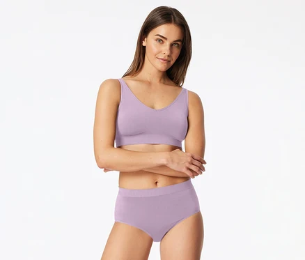 Femme portant une bralette lavande clair et une culotte assortie, les bras croisés, regardant devant elle.