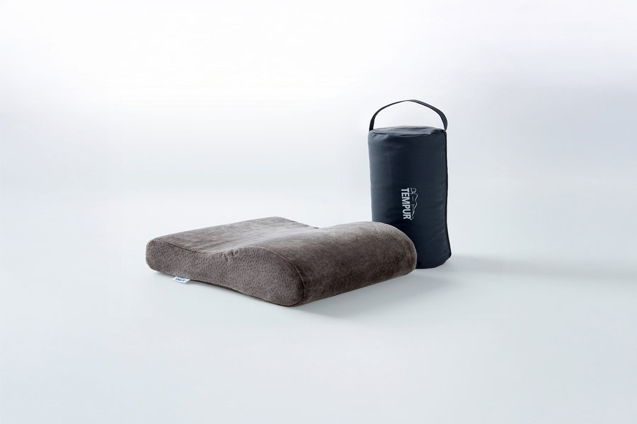 Graues, konturiertes ergonomisches Kissen neben einer schwarzen zylindrischen Tragetasche mit weißem TEMPUR Logo.