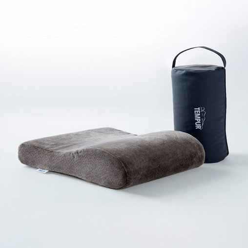 Graues, konturiertes ergonomisches Kissen neben einer schwarzen zylindrischen Tragetasche mit weißem TEMPUR Logo.