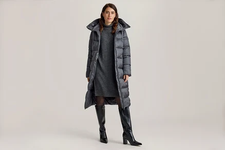Femme portant un manteau matelassé extra-long sur une robe pull grise et des bottes noires montantes.