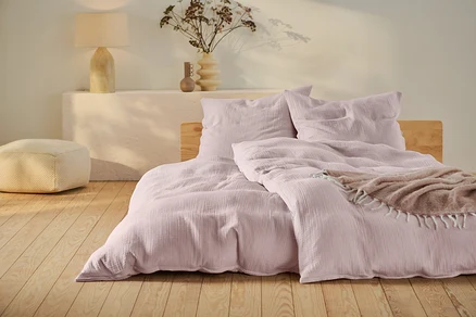 Parure de lit en mousseline rose de taille standard et grande taille sur un lit avec cadre en bois.