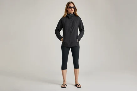 Femme portant des lunettes de soleil et une veste noire en softshell. Elle a les mains dans les poches.