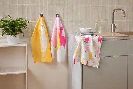 Trois torchons à motifs de lamas sont accrochés dans une cuisine à côté d'un évier et d'une étagère.