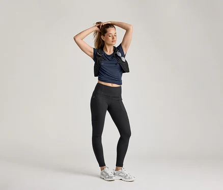 Femme posant en leggings d’extérieur, t-shirt bleu marine et gilet sur fond clair.
