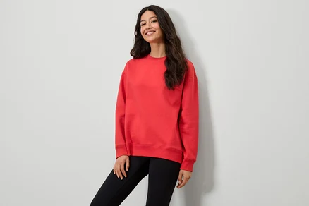 Une femme portant un sweat-shirt rouge et des leggings noirs pose devant un mur blanc.