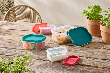 Plusieurs récipients de stockage transparents avec des couvercles colorés sont posés sur une table en bois.