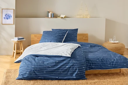 Lit avec des draps rayés bleu et blanc et un motif de nœuds. Sur la table de chevet, il y a des livres et une lampe en forme de bateau.