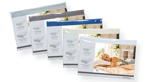 Fünf verpackte TEMPUR Kissenbezüge, diagonal angeordnet, in Hellblau, Dunkelgrau, Blau, Creme und Pfirsichfarben. Die vorderste pfirsichfarbene Verpackung zeigt eine blonde Frau, die auf einem Kissen schläft.