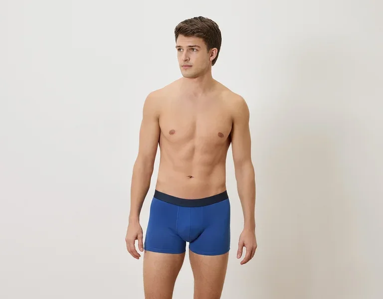 Homme torse nu portant un boxer bleu sur un fond blanc.