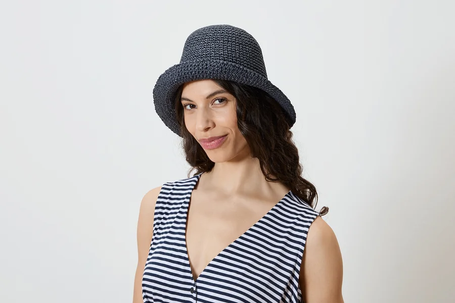 Une femme aux cheveux ondulés foncés porte un chapeau en crochet bleu marine et un débardeur rayé.