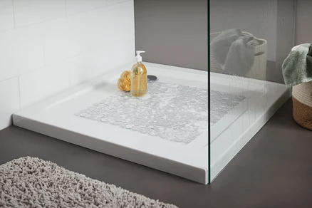Receveur de douche avec un tapis de douche transparent. Sur le receveur se trouvent une éponge de bain jaune et un flacon avec pompe.