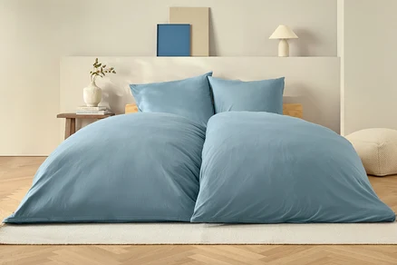 Couette bleue et deux oreillers sur un lit sur un tapis blanc.