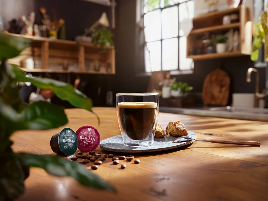 Une tasse de café est posée sur une table à côté de deux capsules Cafissimo Barista.