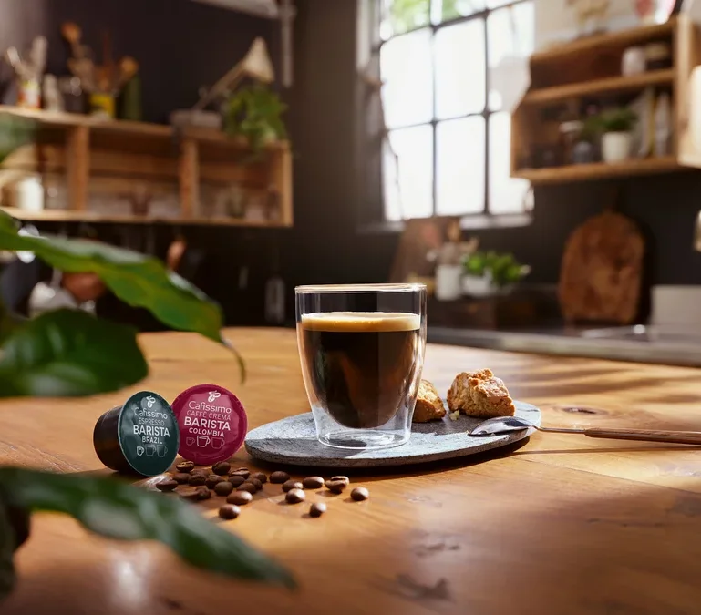 Une tasse de café est posée sur une table à côté de deux capsules Cafissimo Barista.