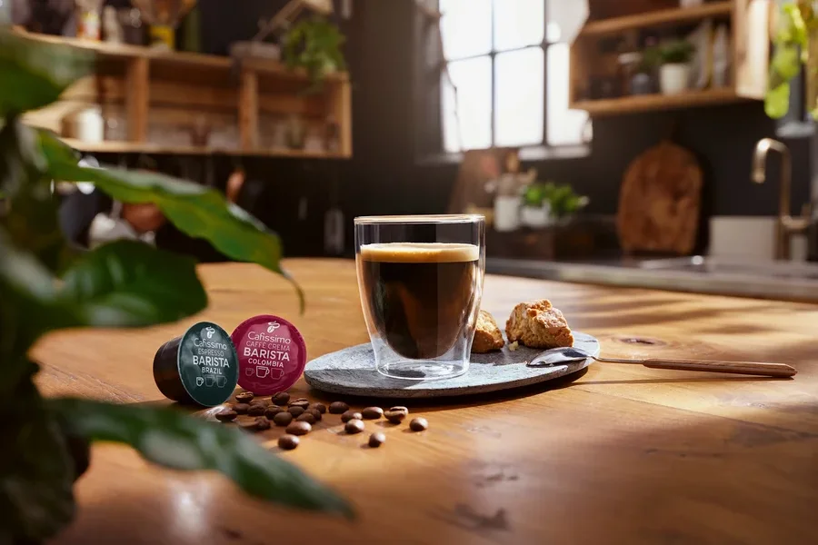 Une tasse de café est posée sur une table à côté de deux capsules Cafissimo Barista.