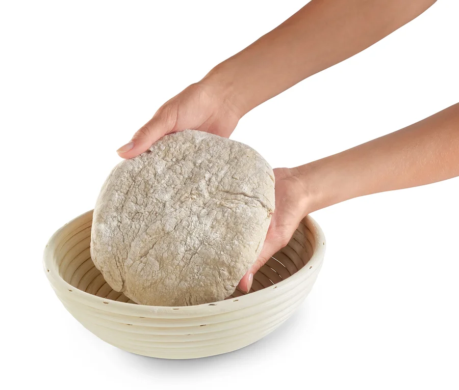 Deux mains placent une boule de pâte dans un banneton rond.