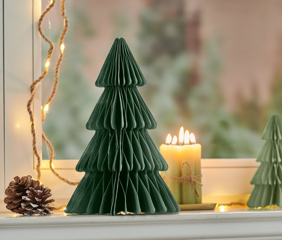 Un arbre en papier pliable moyen est placé à côté d'une bougie allumée et d'une pomme de pin.
