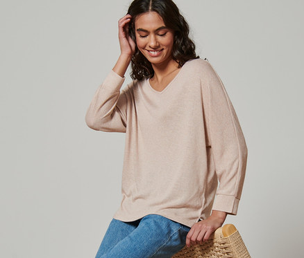 Femme assise sur un fauteuil en osier portant un t-shirt à manches chauve-souris.