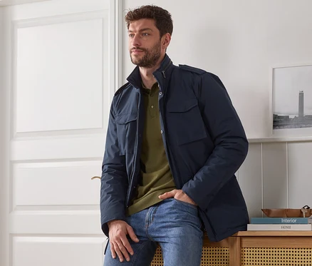 Un homme est assis sur une armoire et porte une veste bleue.