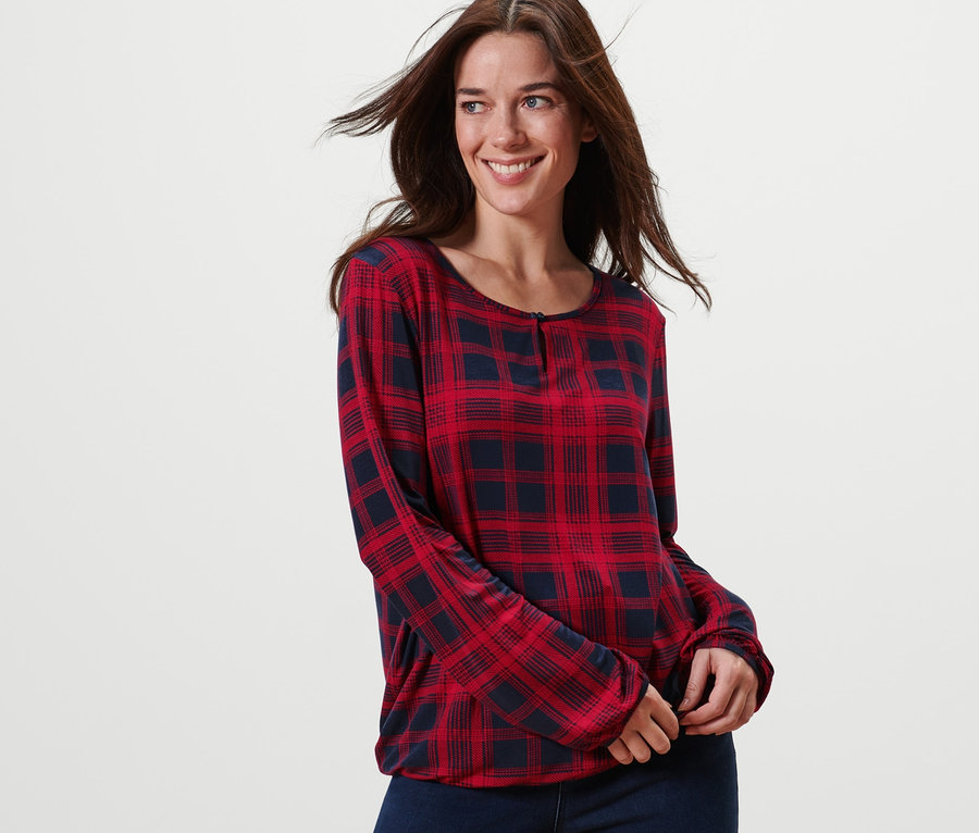 Une femme souriante pose en blouse à carreaux.