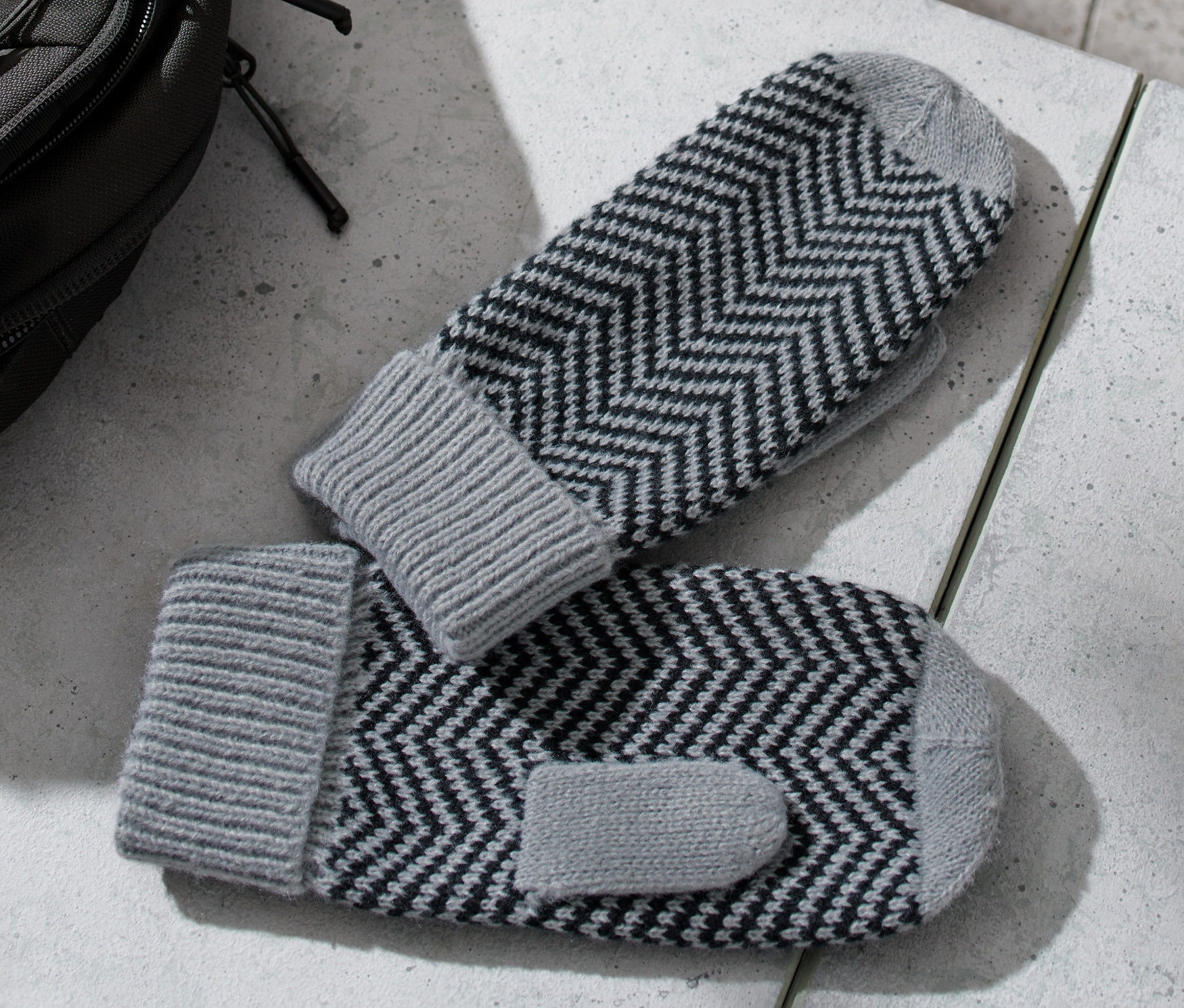 Sur une table se trouvent des moufles en maille, à côté d'elles un sac à dos et une bouteille d'eau.