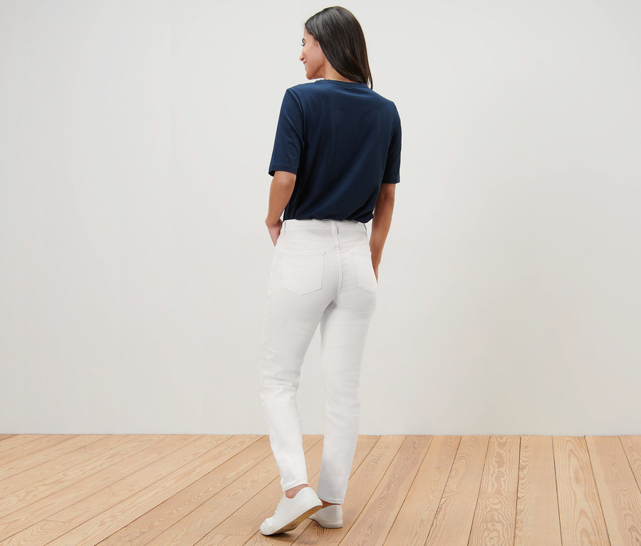 Une femme pose, de dos, en jean – Fit « Kira », t-shirt et baskets.